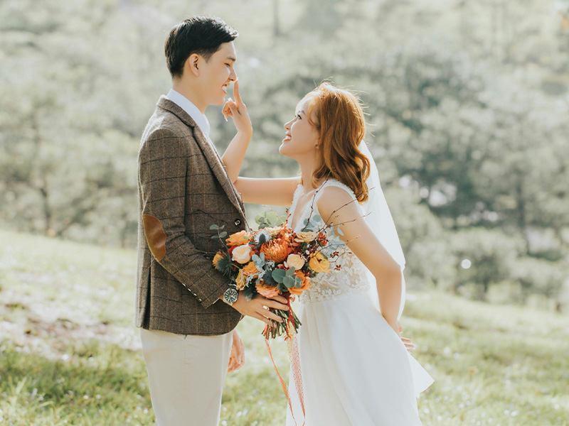 Asian bride and groom in light filled country scene with the bride playfully touching the grooms nose smiling